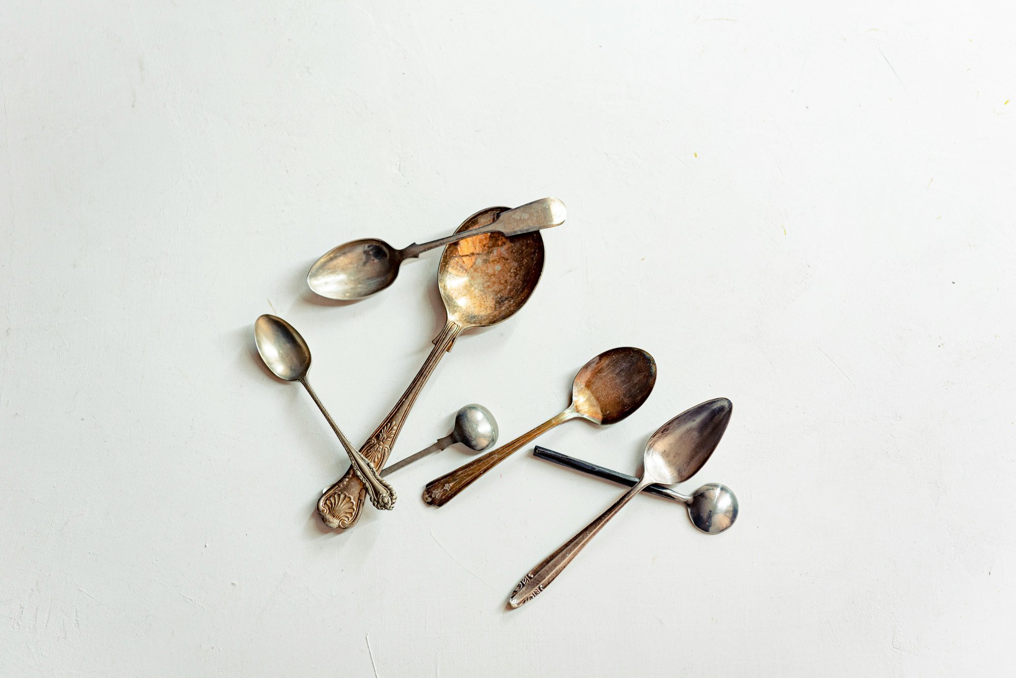 A scattered collection of vintage silver spoons on a pale background